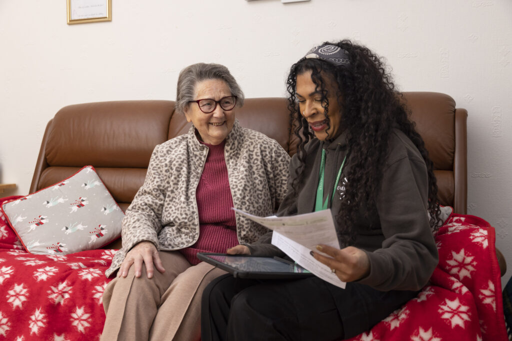 What We Do: Photo of a woman sitting on a couch with an older women engaging in a conversation about energy.