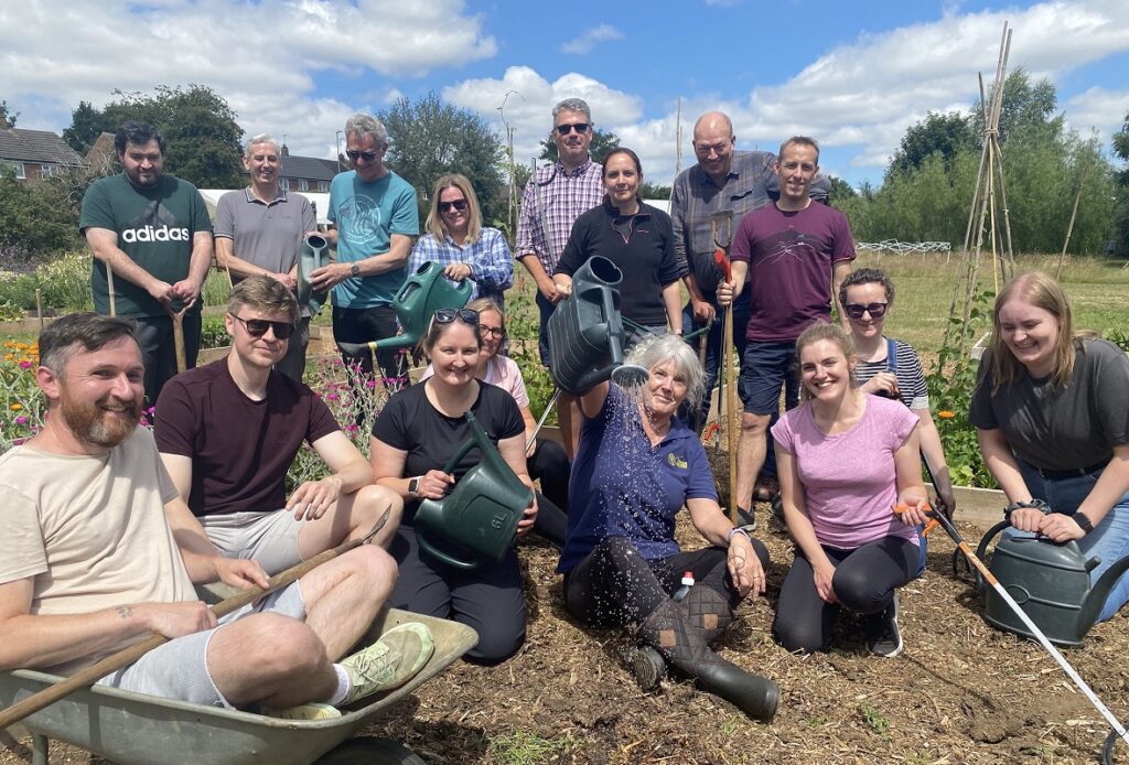 What We Do: Photo of a large group of people in an outdoor allotment holding gardening tools.