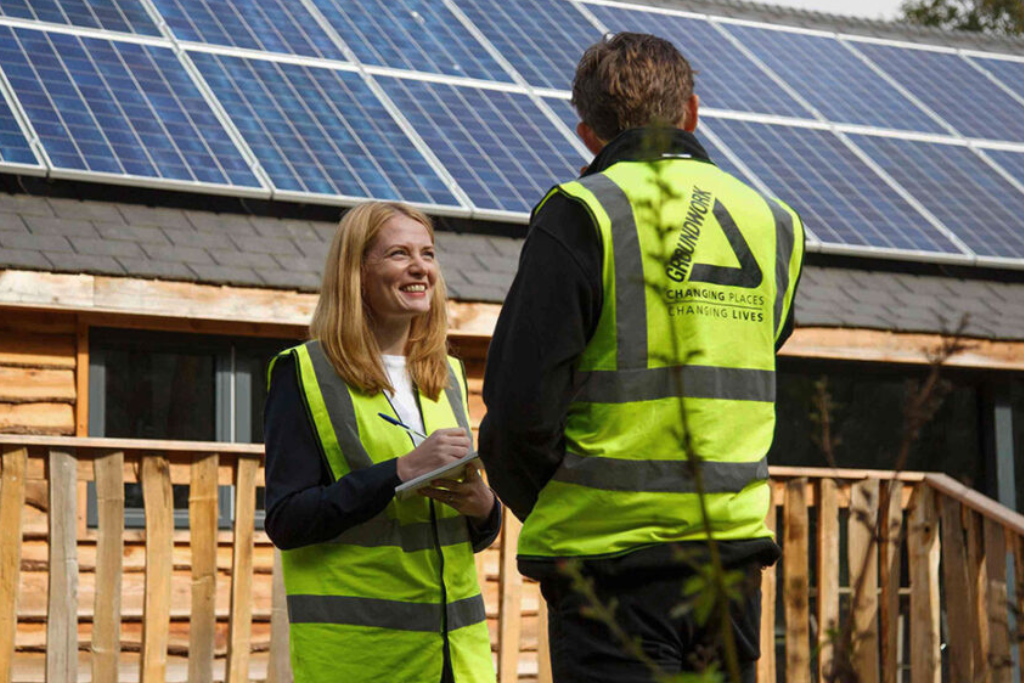 A male and female in high vis jackets stood in front of a building with solar panels on its roof.